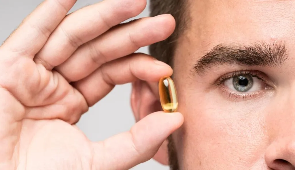 Hombre mostrando pequeña cápsula de suplementos