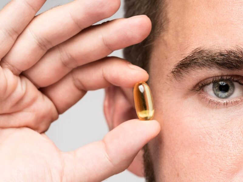 Hombre mostrando pequeña cápsula de suplementos